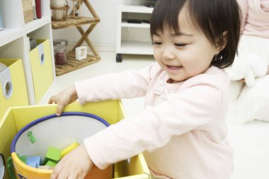 Küçük Asyalı kız kutuda oyuncaklarla oynuyor. 