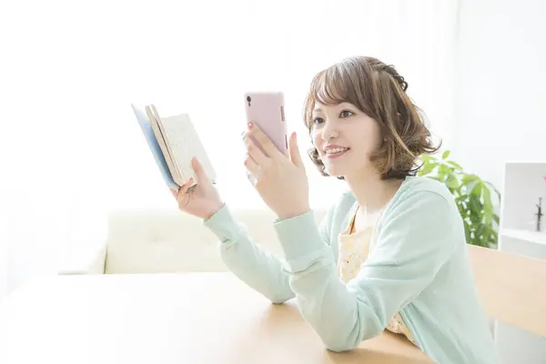 Jong Aziatisch Vrouw Met Boek Met Behulp Van Smartphone Thuis — Stockfoto