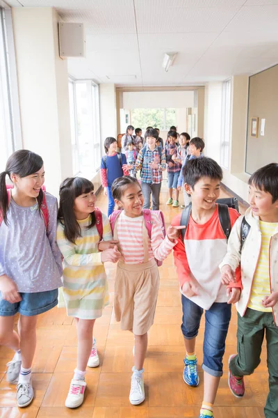 Okul koridorunda sırt çantalı bir grup Japon çocuk yürüyor. 