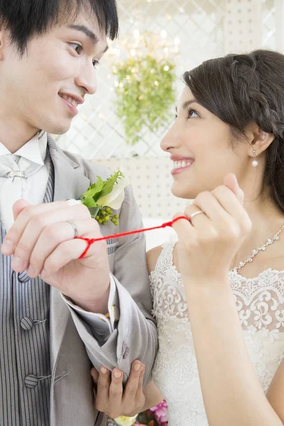 赤いひもで結ばれた指が付いている美しい幸せな若い結婚式のカップル — ストック写真