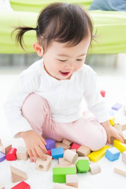 Anaokulunun zemininde renkli oyuncak bloklarıyla oynayan Asyalı çocuk.