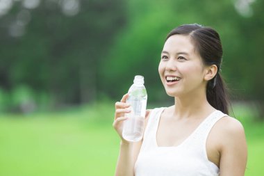 Yeşil yaz parkında gündüz vakti su içen güzel Japon kadın. 