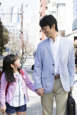 Asyalı baba ve kızı şehirde el ele tutuşuyorlar.