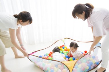 Anne ve kızları renkli toplarla dolu oyun parkında.  