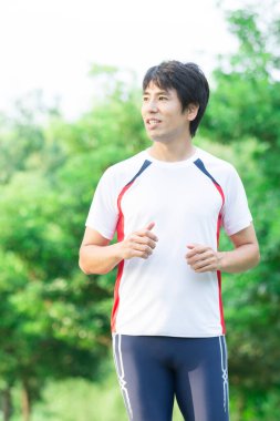 Genç yakışıklı Asyalı adam parkta koşuyor. 