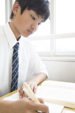 Asyalı öğrenci sınıfta deftere bir şeyler yazıyor.