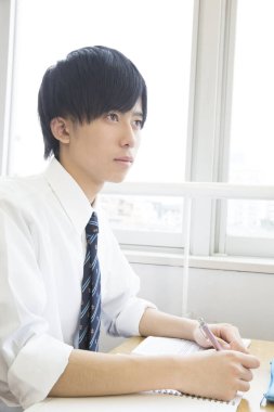 Erkek öğrenci masada oturuyor ve tahtaya bakıyor. 