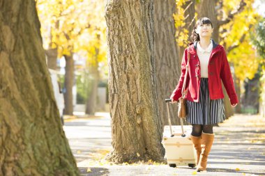 Sonbahar parkında bavullu genç Asyalı kız.