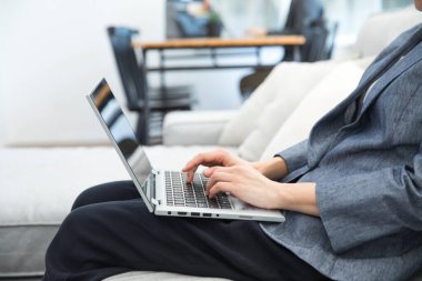 Evde kanepede dizüstü bilgisayar kullanan genç kadın