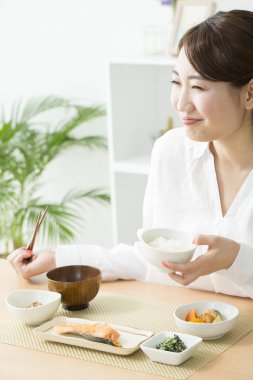Asyalı kadın evde çubuklarla yemek yiyor.