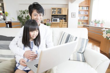 Evde dizüstü bilgisayar kullanan mutlu bir Asyalı aile.