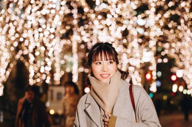 Sonbahar elbiseli güzel Japon kadın sokakta oturuyor, aydınlanmış şehir arka planında. 