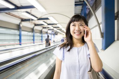 Tren istasyonunda cep telefonu olan genç Asyalı kadın.