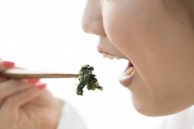 Asyalı kadın evde çubuklarla yemek yiyor.