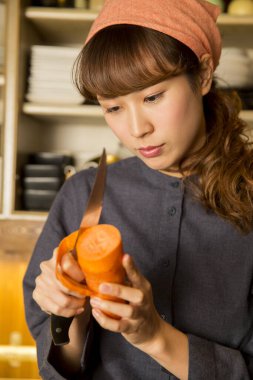 Asyalı genç bayan garson mutfakta havuç soyuyordu.