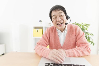 Evde çalışan kulaklıklı ve laptoplu Asyalı bir adam.