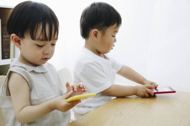 Evde akıllı telefonlarla oynayan iki küçük Asyalı çocuk.