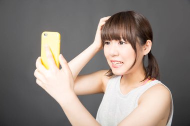 Genç Asyalı kadın gri arka planda cep telefonuyla selfie çekiyor. 