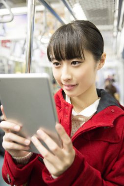 Metroda tablet kullanan Asyalı kadın.