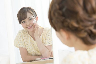 Aynaya gülümseyen bir kadın makyaj yapıyor