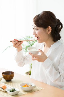 Asyalı kadın evde çubuklarla yemek yiyor.