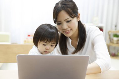 Genç anne ve küçük kızı evde dizüstü bilgisayar kullanıyorlar.