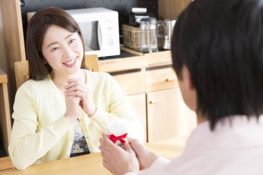 Asyalı genç bir kadın erkekten hediye paketi alıyor. 