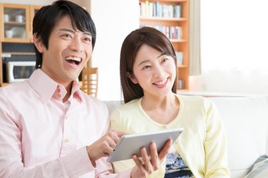 Asyalı genç çift tablet kullanıyor ve gülümsüyor. 