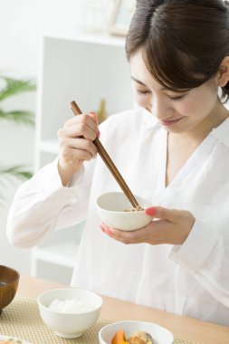 Asyalı kadın evde çubuklarla yemek yiyor.