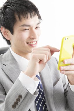 Genç Asyalı işadamı ofiste akıllı telefon kullanıyor.