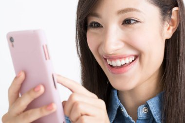 Asyalı kadın gülümseyerek cep telefonunu tutuyor.