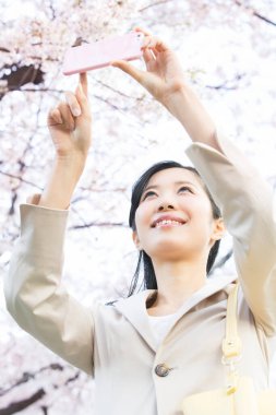 Genç ve güzel Asyalı bir kadın bahar parkında telefonla fotoğraf çekiyor.   