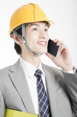 Genç Japon iş adamının yakın plan portresi. Kasketli ve telefonla konuşuyor.