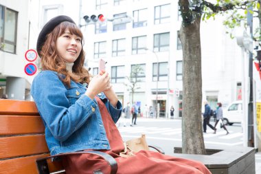 Kadın bankta oturuyor ve cep telefonu kullanıyor.