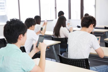 Genç Asyalı öğrenciler sınıfta akıllı telefon kullanıyorlar.