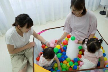 Anne ve kızları renkli toplarla dolu oyun parkında.  