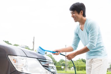 Adam dışarıda mavi fırçayla araba yıkıyor.