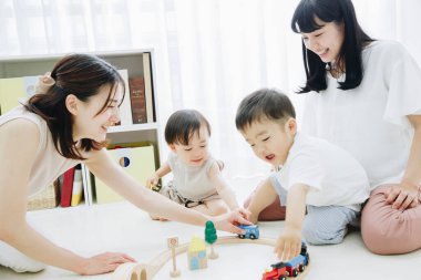 Neşeli Asyalı anneler ve çocuklar oturma odasında oynuyor.