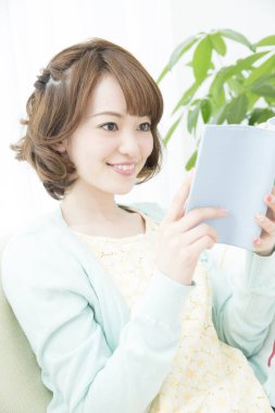 Genç Asyalı kadın evde kitap okuyor.