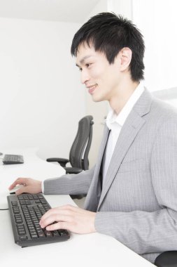 Ofiste bilgisayarla çalışan gülümseyen Asyalı çalışan