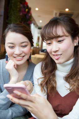 İki arkadaş kafede telefona bakıyor.