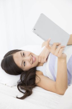 Yatağın üzerinde tablet bilgisayarı olan kadın.