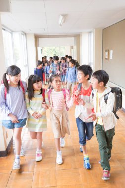 Okul koridorunda sırt çantalı bir grup Japon çocuk yürüyor. 