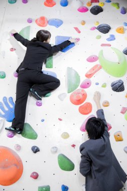 Japon iş kadını ve takım elbiseli iş adamı spor salonunda duvara tırmanıyor. 