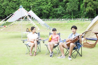 Mutlu Asyalı arkadaşlar kamp parkında müzik aletleri çalıyorlar.