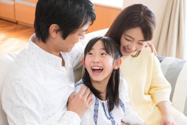 Asyalı anne-baba ve kız evdeki kanepede oturuyor. 