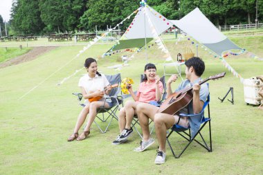 Mutlu Asyalı arkadaşlar kamp parkında müzik aletleri çalıyorlar.