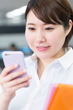 Ofiste akıllı telefon kullanan Asyalı kadın. 