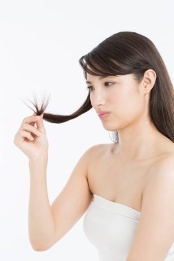 Asyalı kadın uzun saçlarını tutuyor ve hasarlı saç uçlarına bakıyor. 