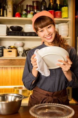 Asyalı garson kadın tabak siliyor.